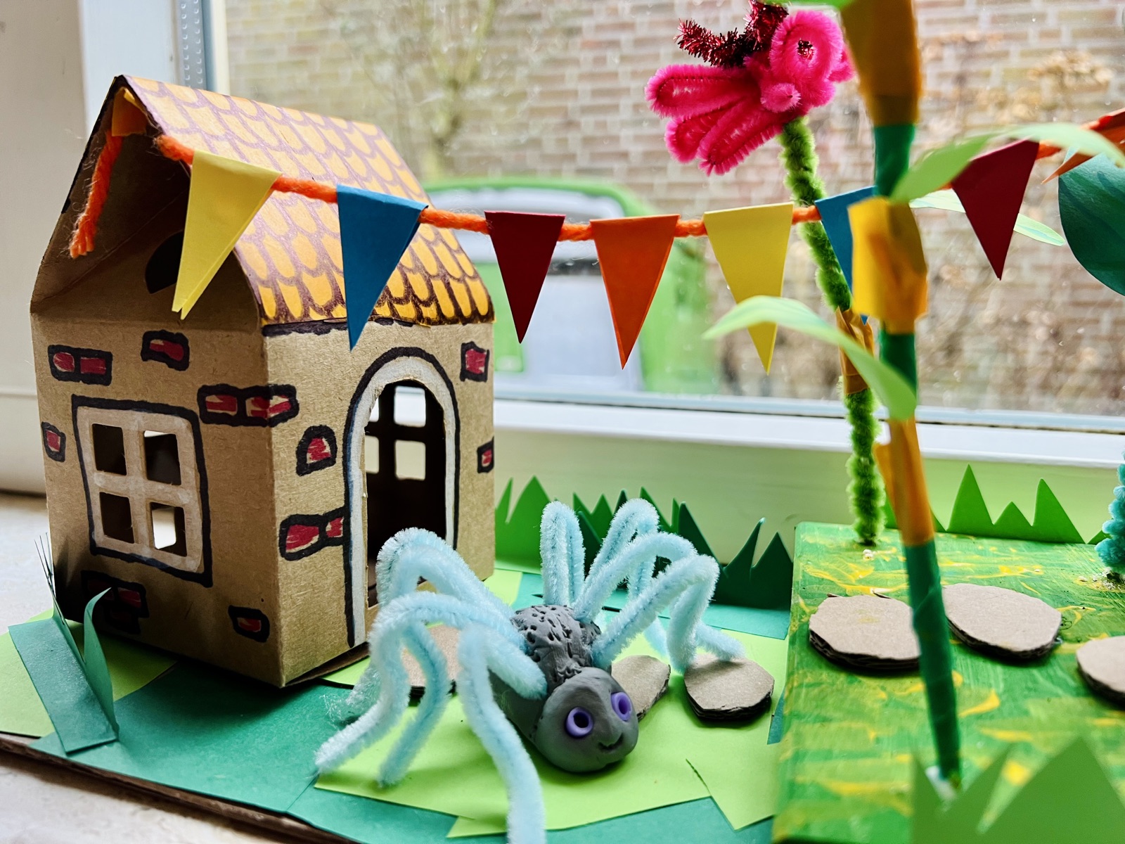 Een knutselwerk met een huisje, vlaggetjes en een spin van pijpenragers