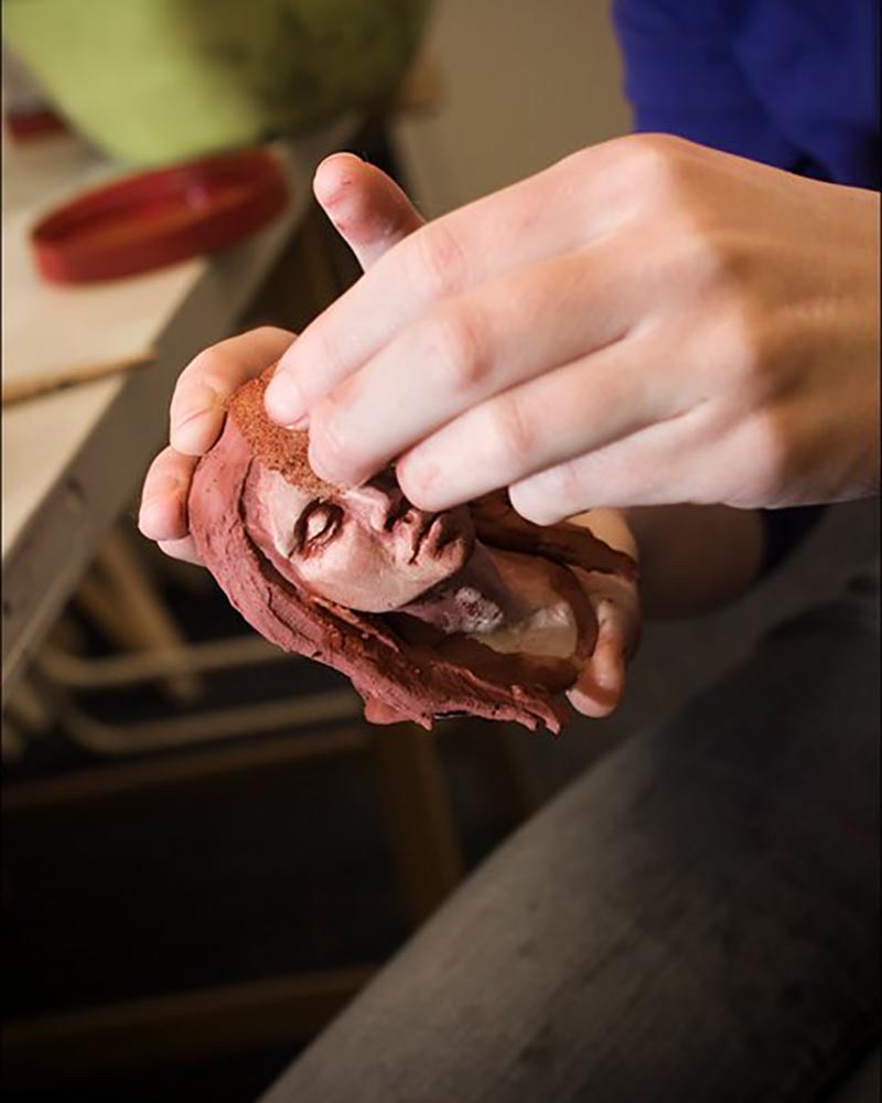 Handen die een hoofdje van klei boetseren